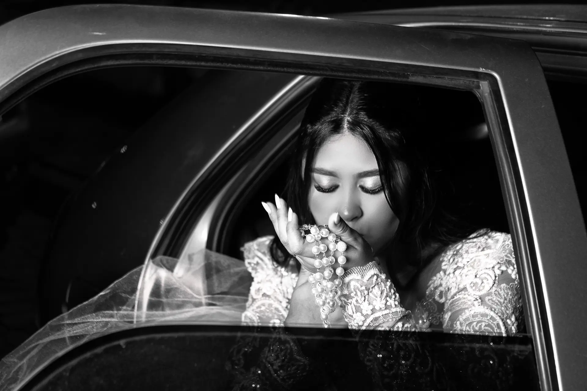 Noiva em preto e branco no carro, com véu e terço — fotografia de casamento no Sul de Minas